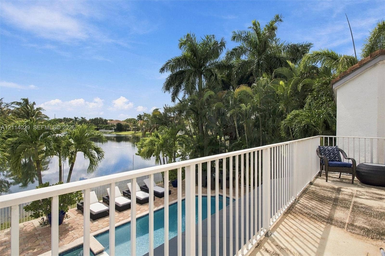 5257 SW 158th Avenue, Miramar, FL 33027 Second-story balcony with white metal railings overlooking a rectangular swimming pool, paver patio, mature palm trees, and a pond