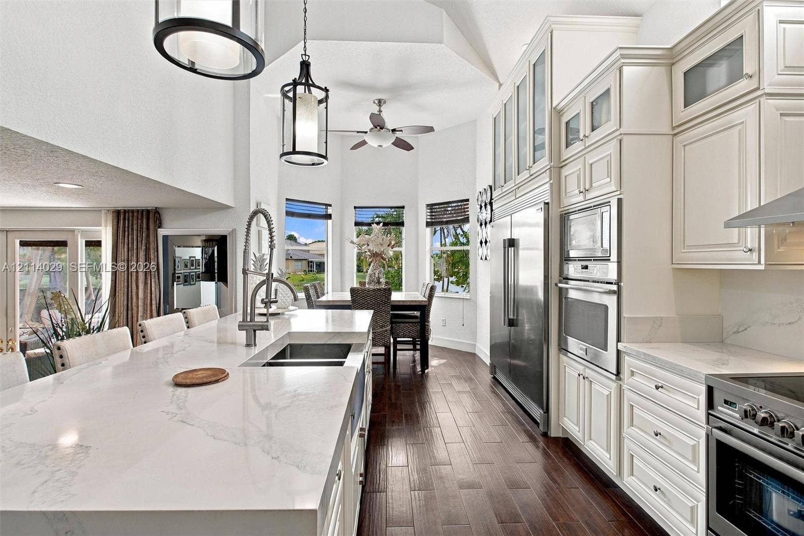 5257 SW 158th Avenue, Miramar, FL 33027 Kitchen featuring a quartz-topped island with an undermount sink, custom cabinetry with glass-front uppers, stainless steel built-in appliances, wood-finish flooring, and vaulted ceilings