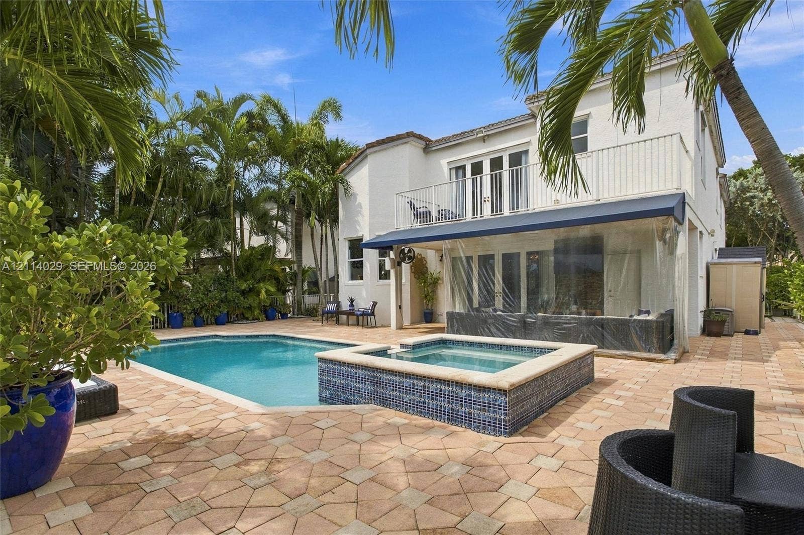 5257 SW 158th Avenue, Miramar, FL 33027 Exterior features including a swimming pool with a raised tiled spa, expansive paver patio, second-story balcony with metal railing, and retractable exterior awning