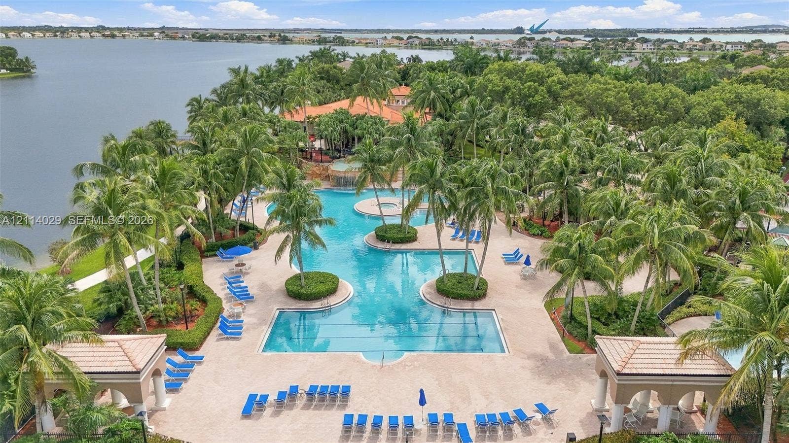 5257 SW 158th Avenue, Miramar, FL 33027 Outdoor swimming pool with integrated spa and rock-feature waterfall, surrounded by concrete decking, palm trees, and two covered cabana structures