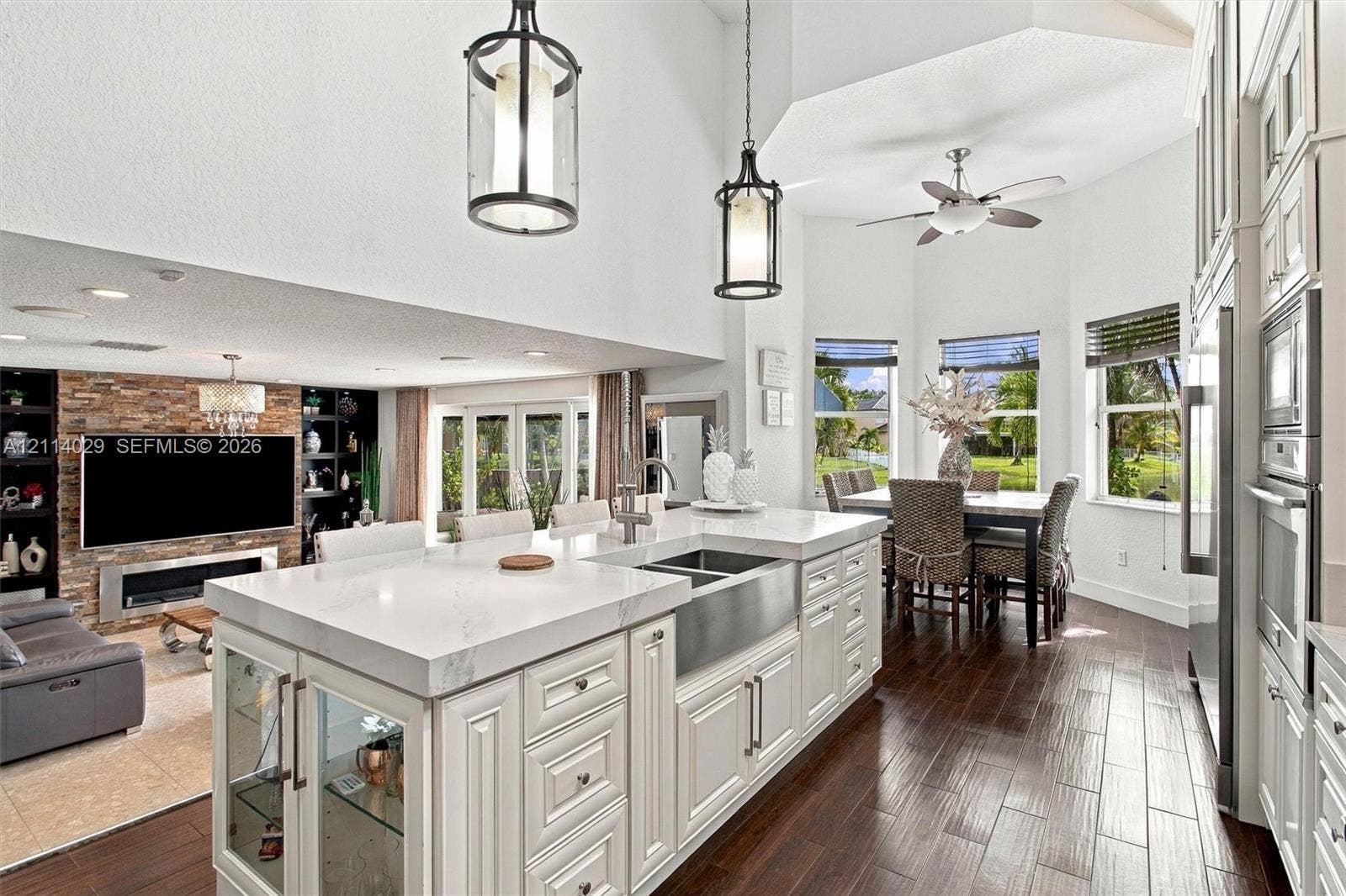 5257 SW 158th Avenue, Miramar, FL 33027 Kitchen featuring a central island with a quartz countertop, stainless steel apron-front sink, white cabinetry with glass-fronted accents, wood-finish flooring, and vaulted ceilings with hanging pendant lighting