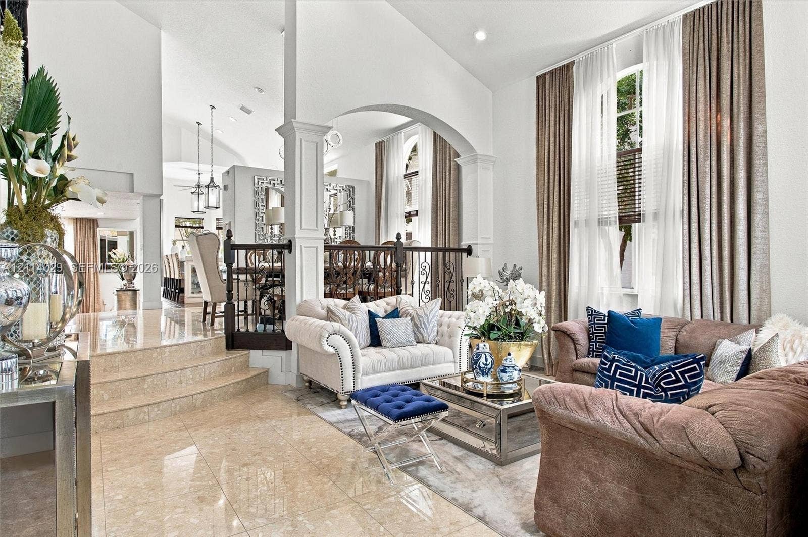 5257 SW 158th Avenue, Miramar, FL 33027 High-ceilinged living area featuring stone-finish tile flooring, arched architectural details, custom wrought-iron railings, and tall windows