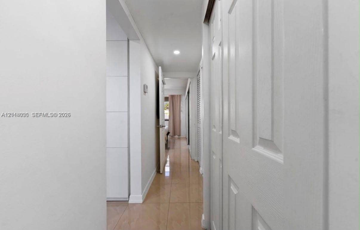 8550 Byron Avenue, #2H, Miami Beach, FL 33141 Hallway featuring light-toned tile flooring, recessed ceiling lighting, and floor-to-ceiling white built-in cabinetry with flush-panel doors