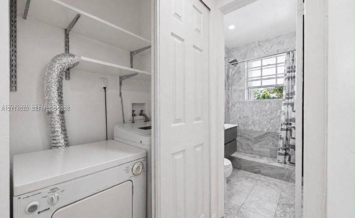 8550 Byron Avenue, #2H, Miami Beach, FL 33141 Laundry area featuring built-in white shelving, and bathroom equipped with stone-finish wall tile, tile flooring, and a window