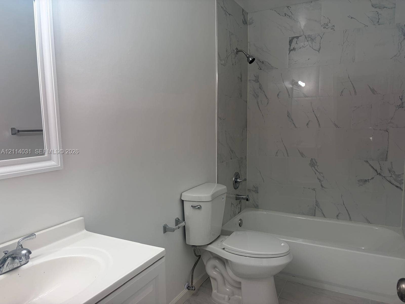 Bathroom featuring a vanity with an integrated sink, framed wall mirror, and a combination tub and shower enclosure with full-height stone-patterned tile surround