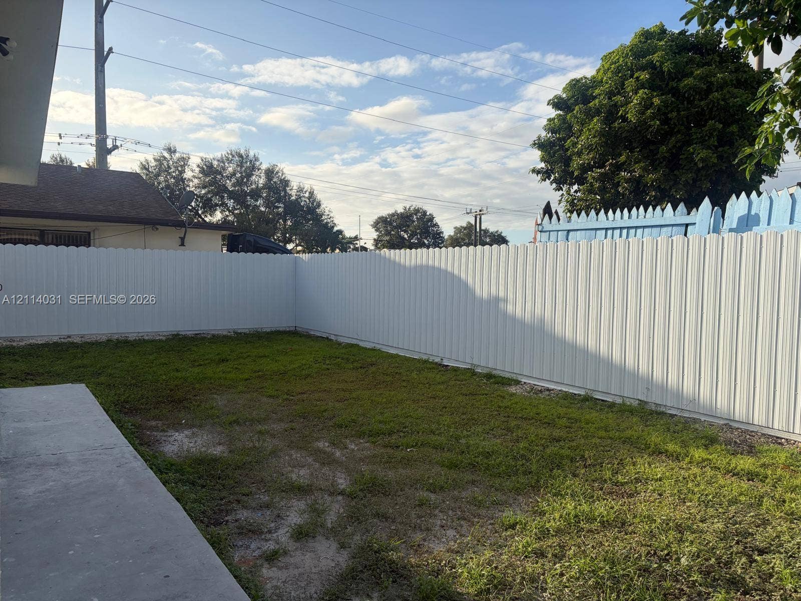 Backyard area featuring a concrete patio, a grass lawn, and white corrugated privacy fencing