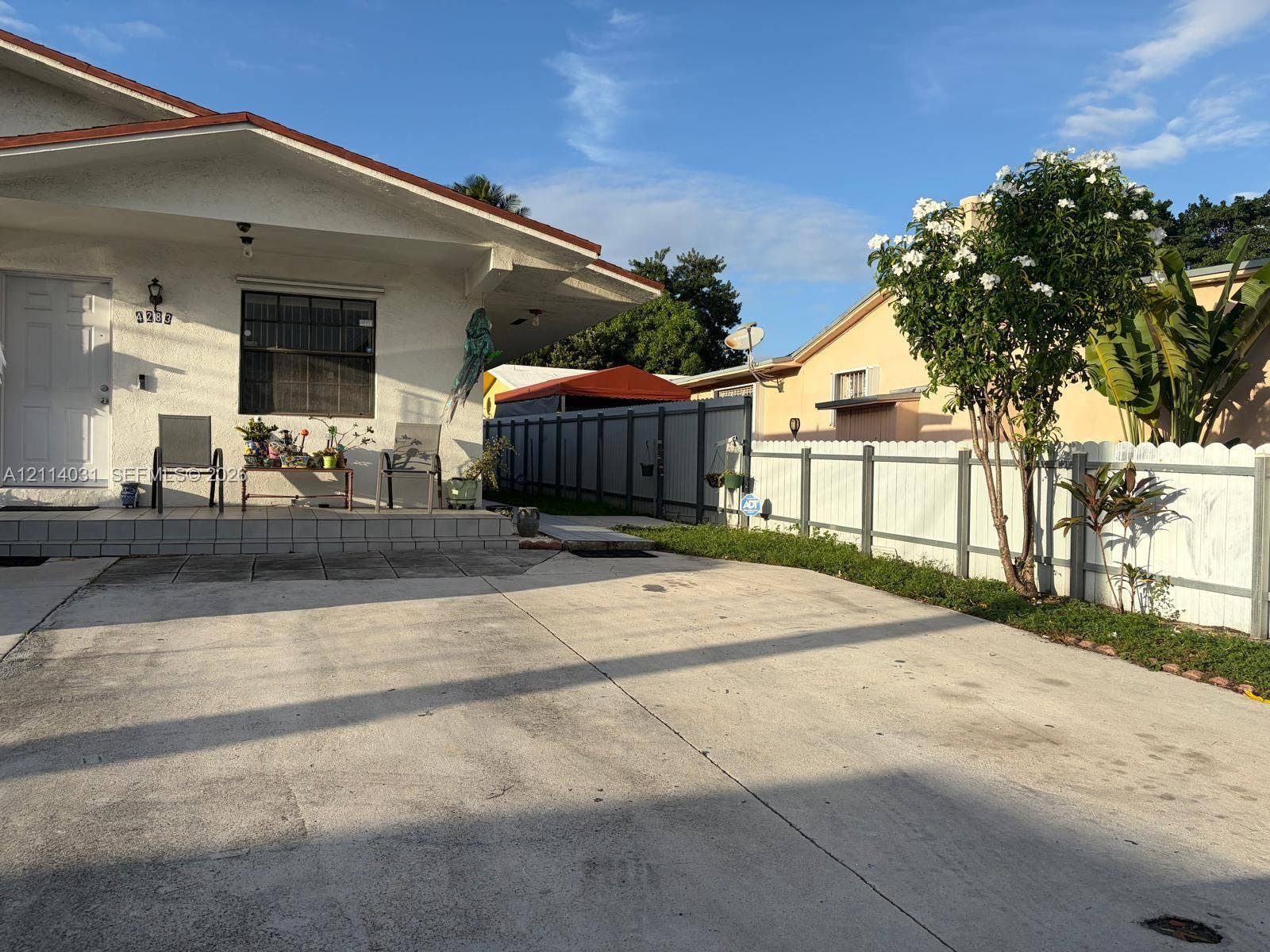 Stucco exterior residence featuring a tiled front porch, concrete driveway, and white picket-style fencing