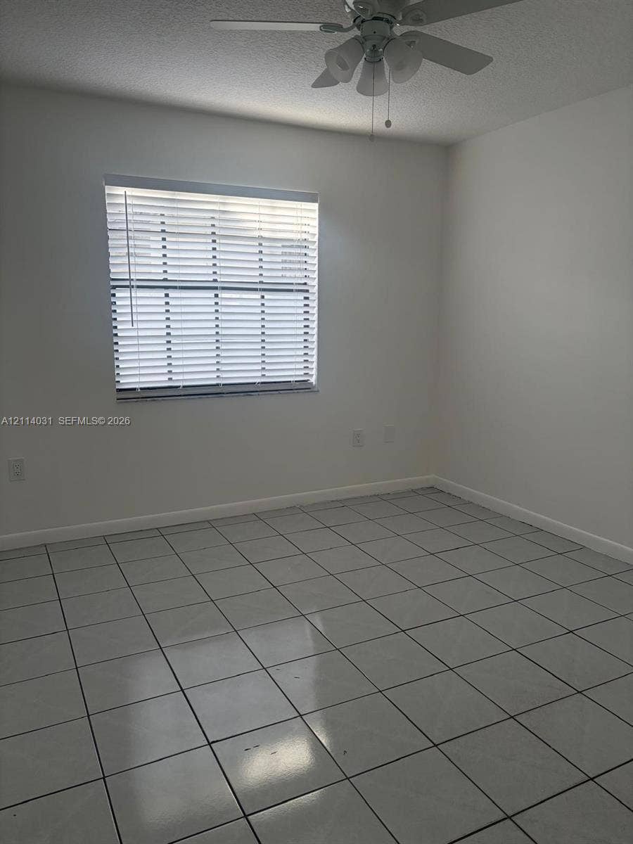 Room featuring neutral wall-to-wall ceramic tile flooring, a window with horizontal blinds, and a ceiling-mounted light fixture with a fan