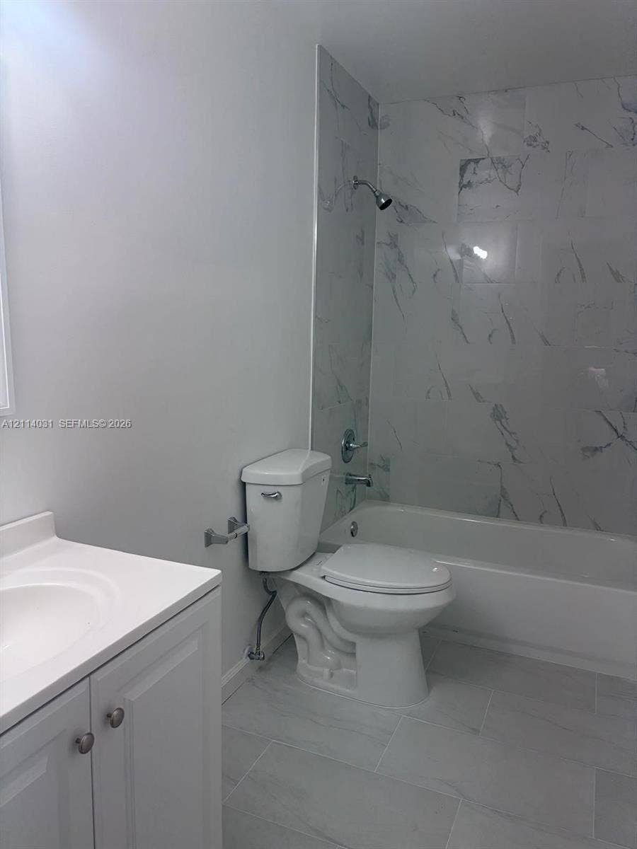 Bathroom featuring large-format tile flooring, vanity with integrated basin, and full-height tiled tub surround