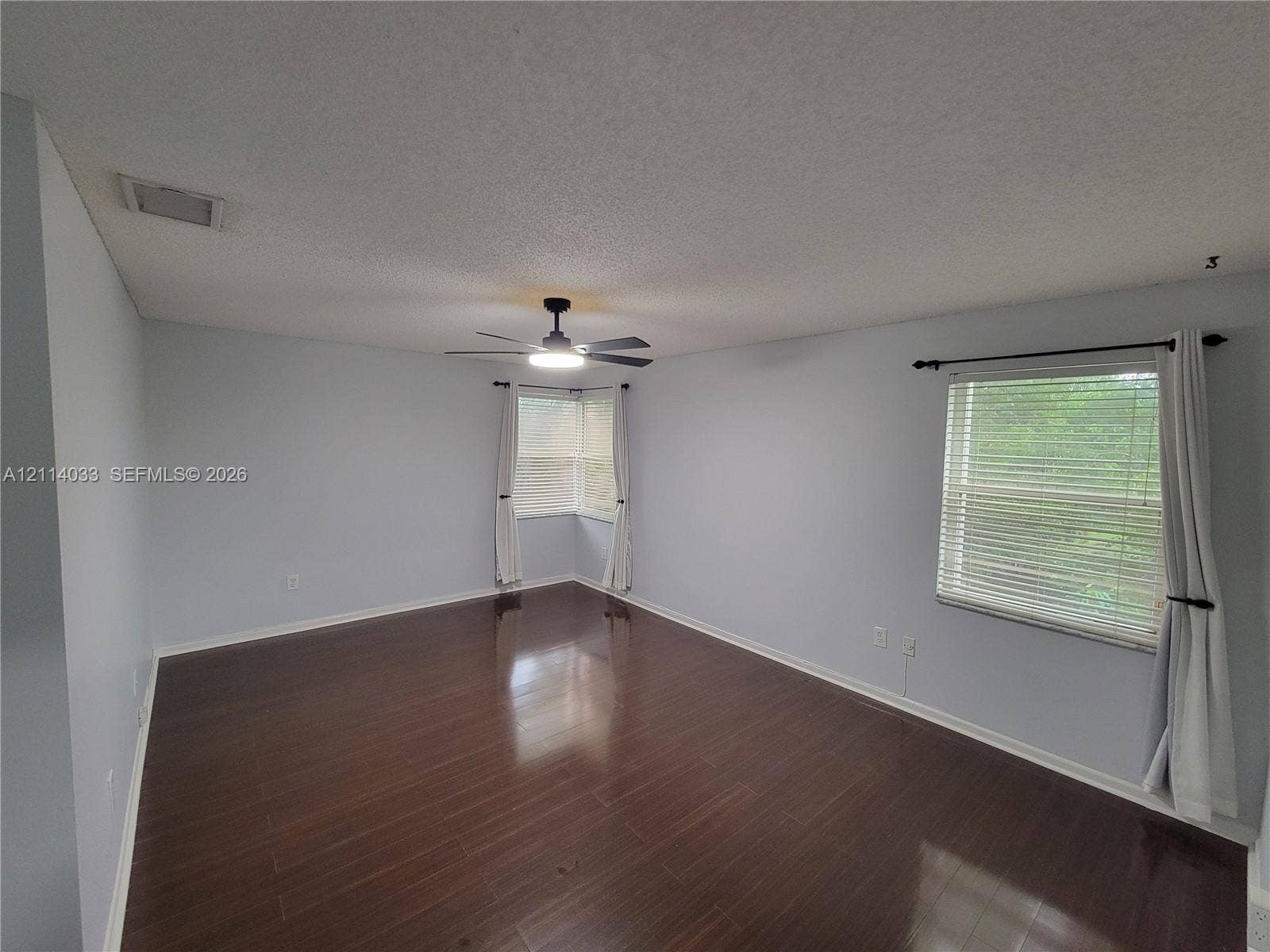 683 NW 88th Drive, Coral Springs, Coral Springs, FL 33071 Spacious room featuring dark wood-finish flooring, a central ceiling fan with an integrated light fixture, dual-window corner configuration, and horizontal window blinds