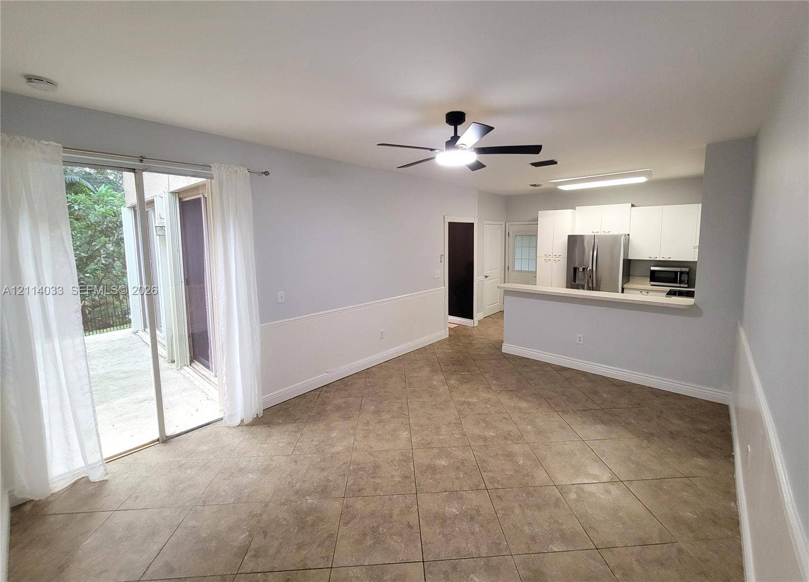 683 NW 88th Drive, Coral Springs, Coral Springs, FL 33071 Large-format tile flooring, kitchen with white cabinetry and stainless steel appliances, breakfast bar, ceiling fan, and sliding glass doors