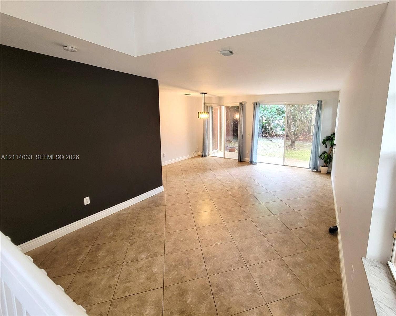 683 NW 88th Drive, Coral Springs, Coral Springs, FL 33071 Spacious room featuring a vaulted ceiling, large-format tile flooring, a prominent accent wall, and dual sliding glass doors