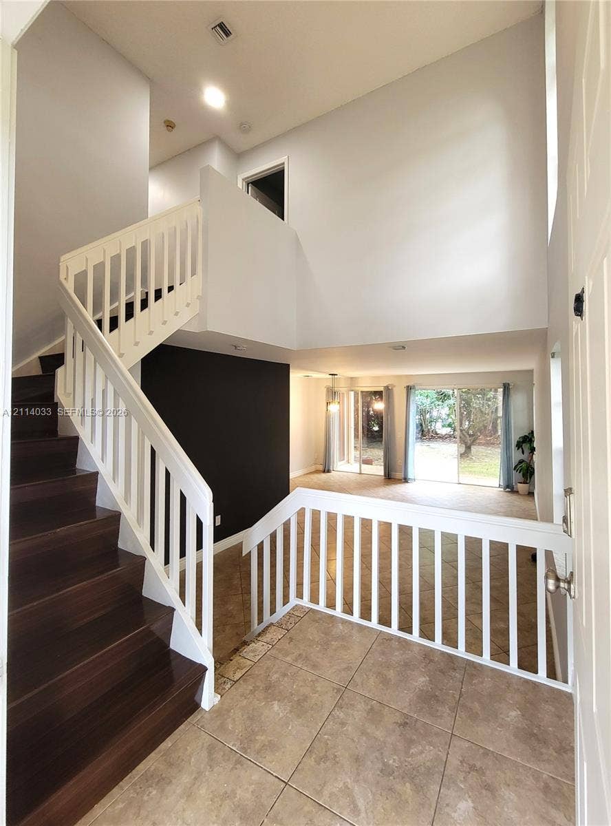683 NW 88th Drive, Coral Springs, Coral Springs, FL 33071 Foyer featuring high ceilings, wood-finish staircase treads, white balustrades, large-format tile flooring, and sliding glass doors