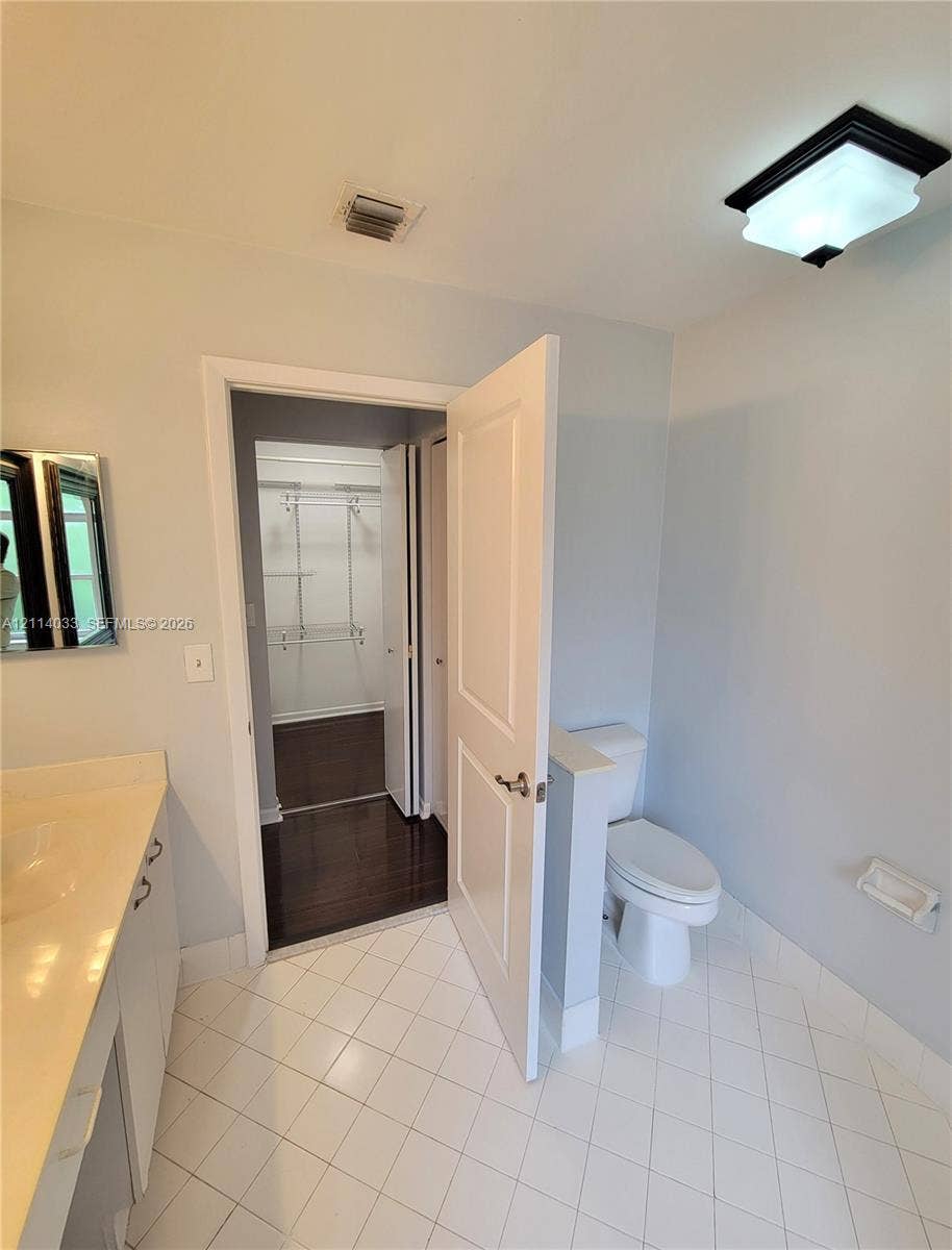 683 NW 88th Drive, Coral Springs, Coral Springs, FL 33071 Bathroom featuring a vanity with integrated sink and countertop, white tile flooring, enclosed water closet with half-wall, and walk-in closet with wire shelving and dark wood-finish flooring
