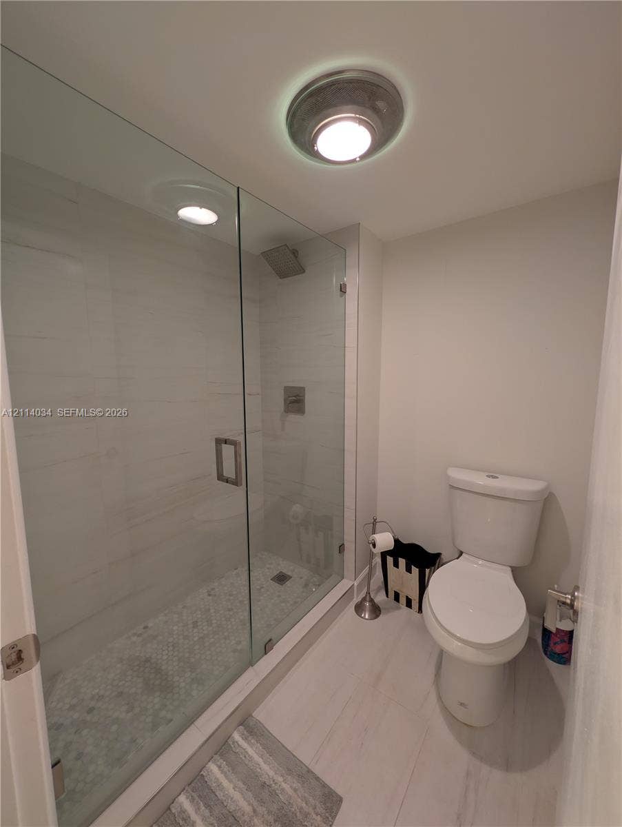 8460 Casa Del Lago, #H, Boca Raton, Boca Raton, FL 33433 Walk-in shower featuring a glass enclosure, light-toned wall tile, and a decorative pebble-style floor, paired with a porcelain commode