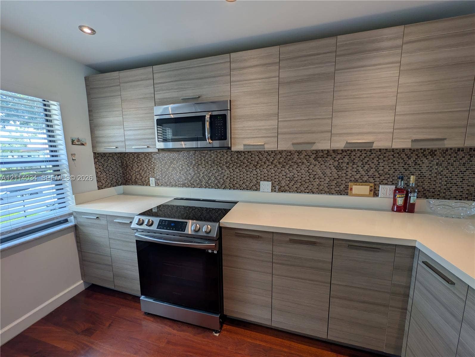8460 Casa Del Lago, #H, Boca Raton, Boca Raton, FL 33433 Kitchen featuring horizontal wood-grain cabinetry, stainless steel appliances, solid surface countertops, and a decorative pebble-tile backsplash
