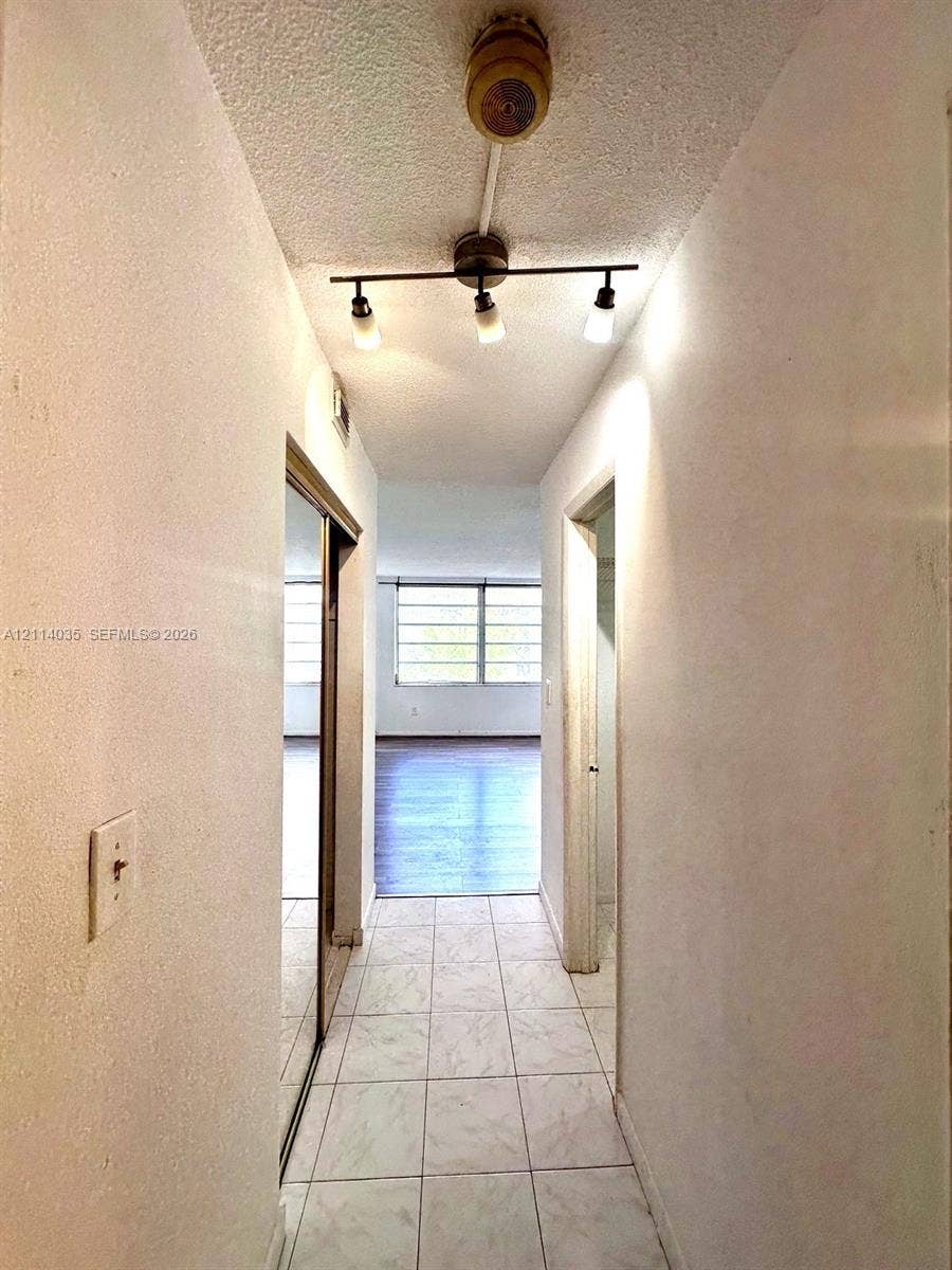 1501 NE 191st Street, #C312, Miami, Miami, FL 33179 Hallway featuring light-toned tile flooring, a three-bulb adjustable track light fixture, and floor-to-ceiling mirrored closet doors