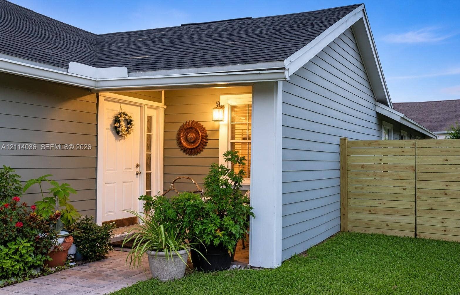 14035 SW 103rd Terrace, Miami, FL 33186 Covered entryway featuring horizontal lap siding, a paneled door with glass sidelight, exterior wall-mounted lighting, and a stone-paver walkway
