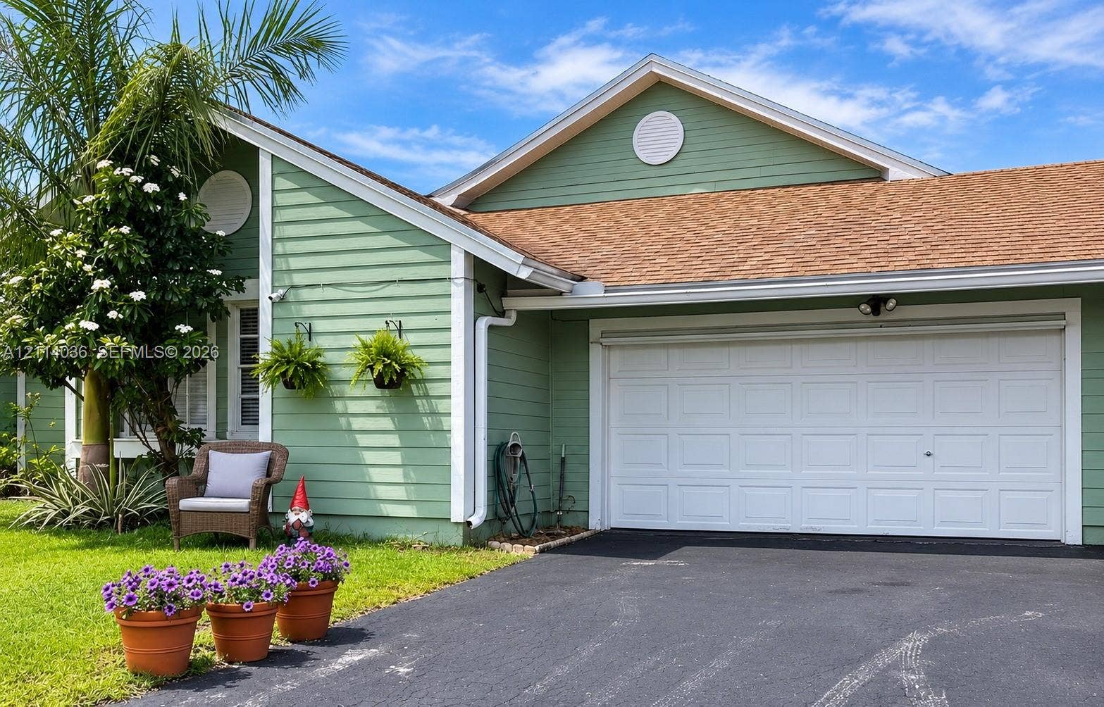 14035 SW 103rd Terrace, Miami, FL 33186 Exterior featuring horizontal lap siding, shingle roof, attached garage with white paneled door, circular gable vents, and paved driveway
