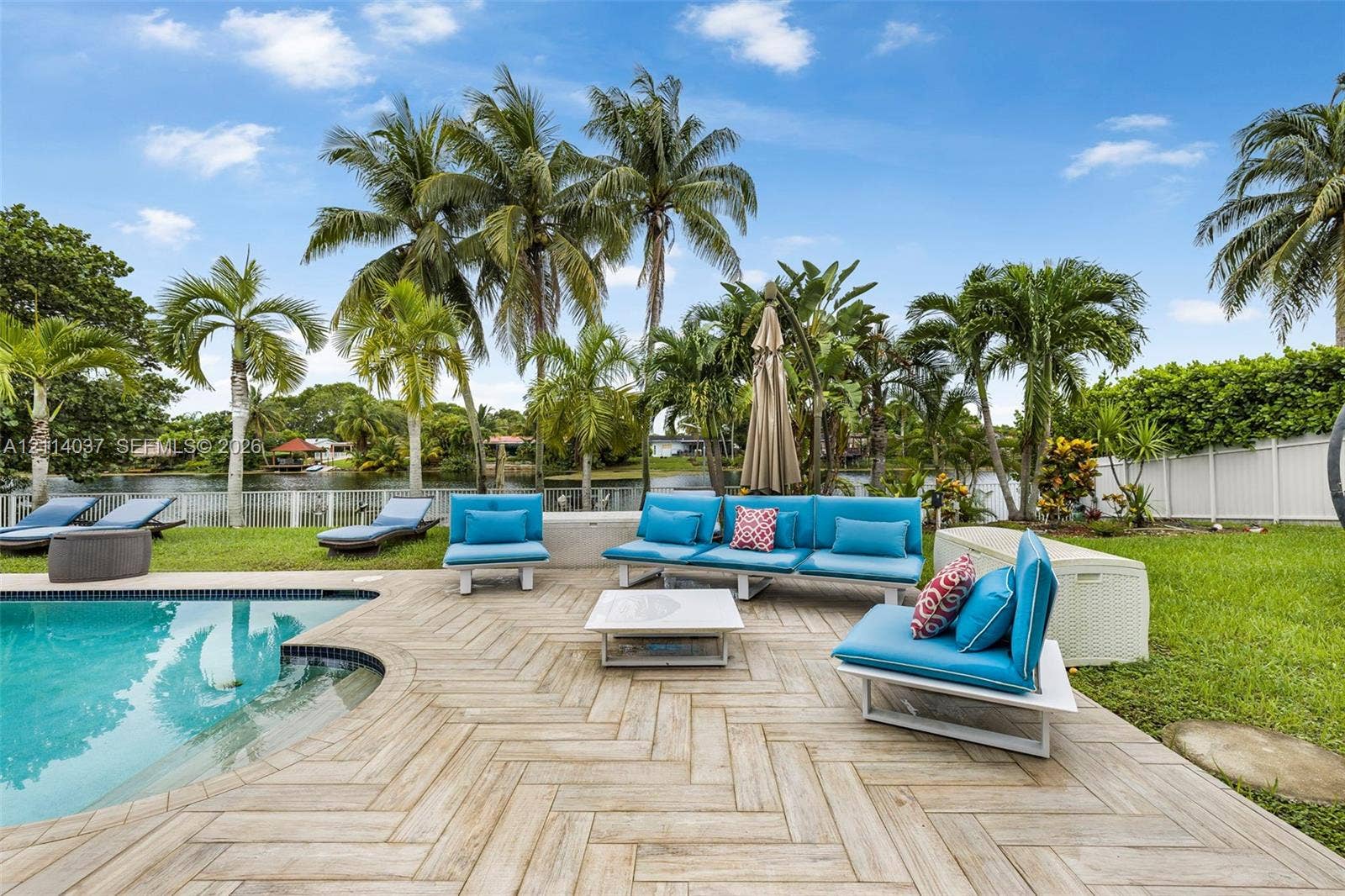 8436 SW 143rd Avenue, Miami, FL 33183 Waterfront backyard featuring a swimming pool with a stepped entry, herringbone-patterned tile decking, mature palm trees, and a white privacy fence
