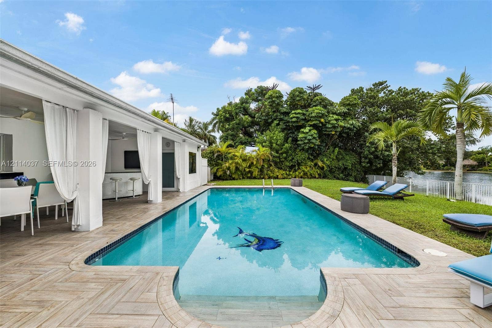 8436 SW 143rd Avenue, Miami, FL 33183 Rectangular swimming pool featuring a decorative floor inlay, bordered by herringbone-patterned tile decking and a covered outdoor patio with structural columns