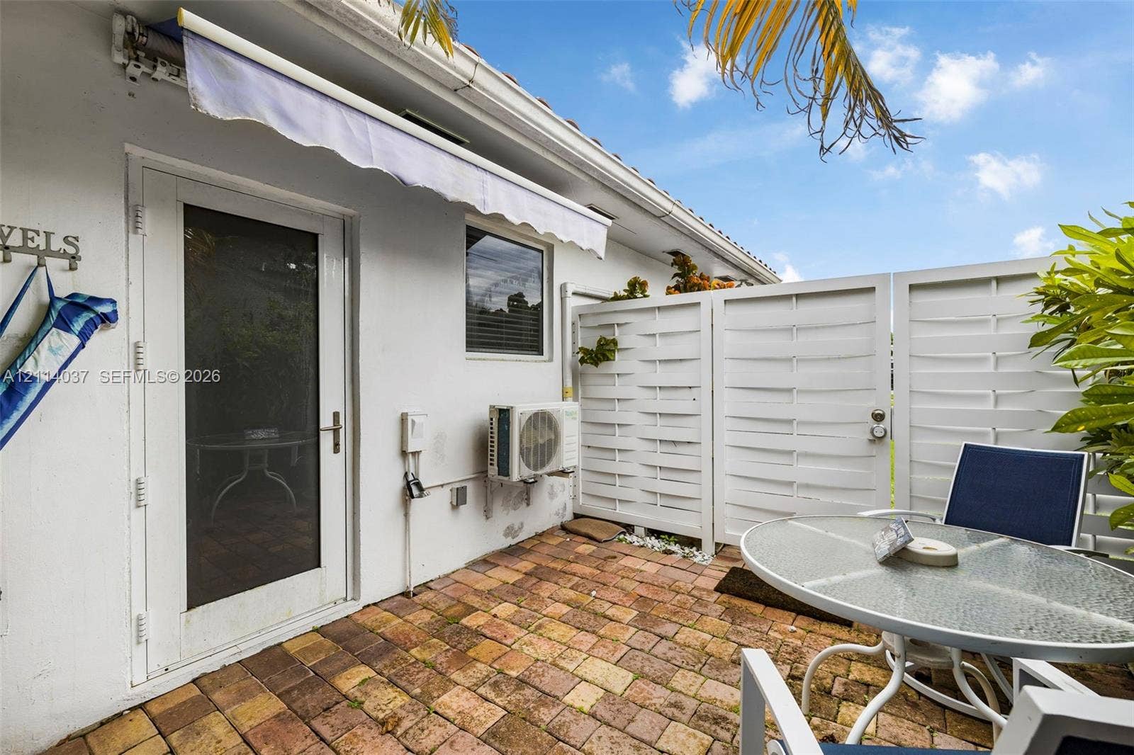 8436 SW 143rd Avenue, Miami, FL 33183 Private patio featuring brick pavers, a retractable exterior awning, and horizontal-slat privacy fencing