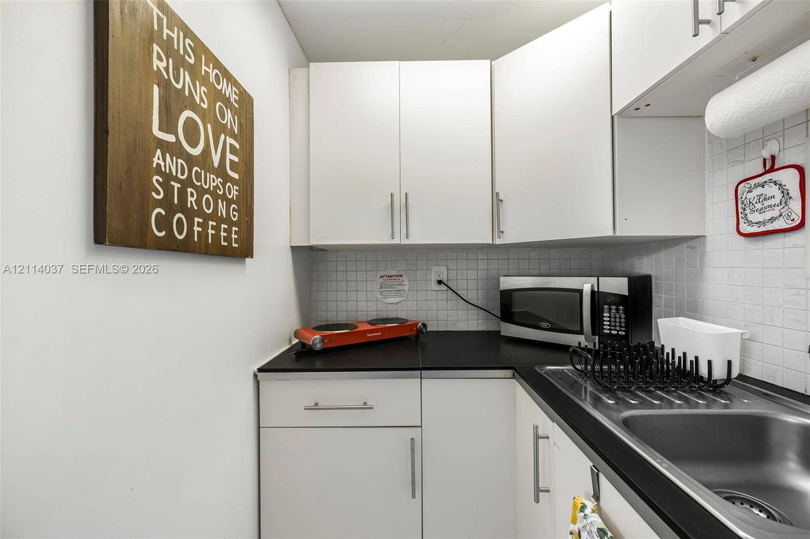 8436 SW 143rd Avenue, Miami, FL 33183 Kitchenette featuring white cabinetry, black countertops, stainless steel sink, and white tiled backsplash
