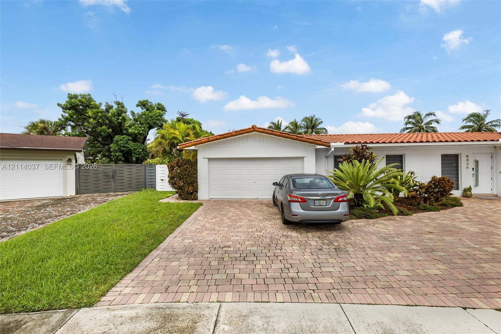8436 SW 143rd Avenue, Miami, FL 33183 Single-story residence featuring a terracotta-tiled roof, white stucco exterior, paved brick driveway, two-car garage, and manicured landscaping