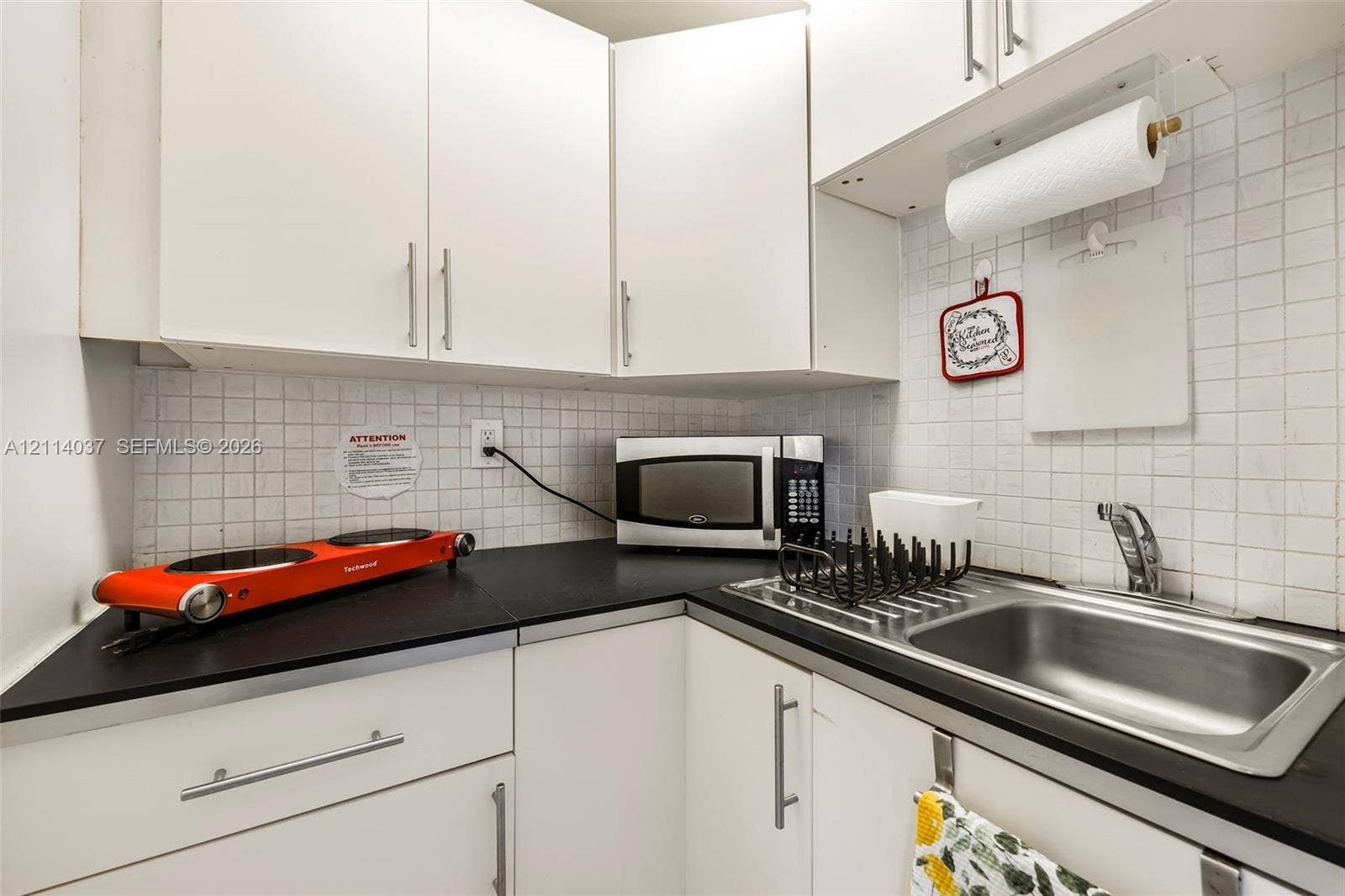 8436 SW 143rd Avenue, Miami, FL 33183 Kitchenette featuring white cabinetry, black countertops, stainless steel sink with a high-arch faucet, and a tiled backsplash