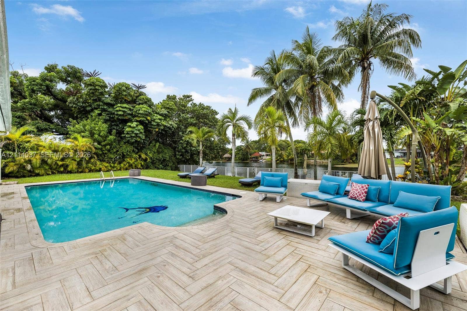 8436 SW 143rd Avenue, Miami, FL 33183 In-ground swimming pool with a herringbone-patterned tile deck, manicured lawn, and mature palm trees along the waterfront