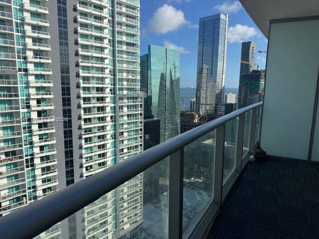 Covered balcony featuring square interlocking floor tiles and a full-height glass railing with a metallic handrail