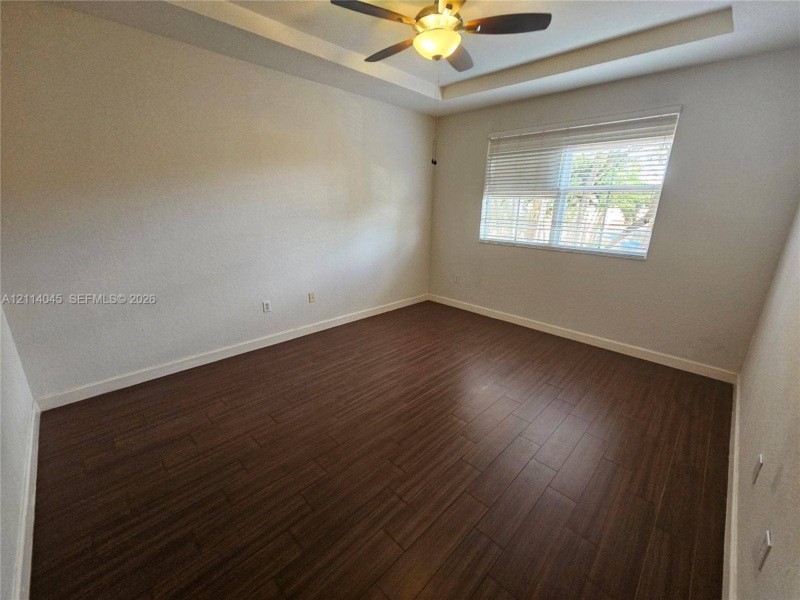 Interior space featuring dark wood-finish flooring, a tray ceiling, and an integrated ceiling fan with light fixture