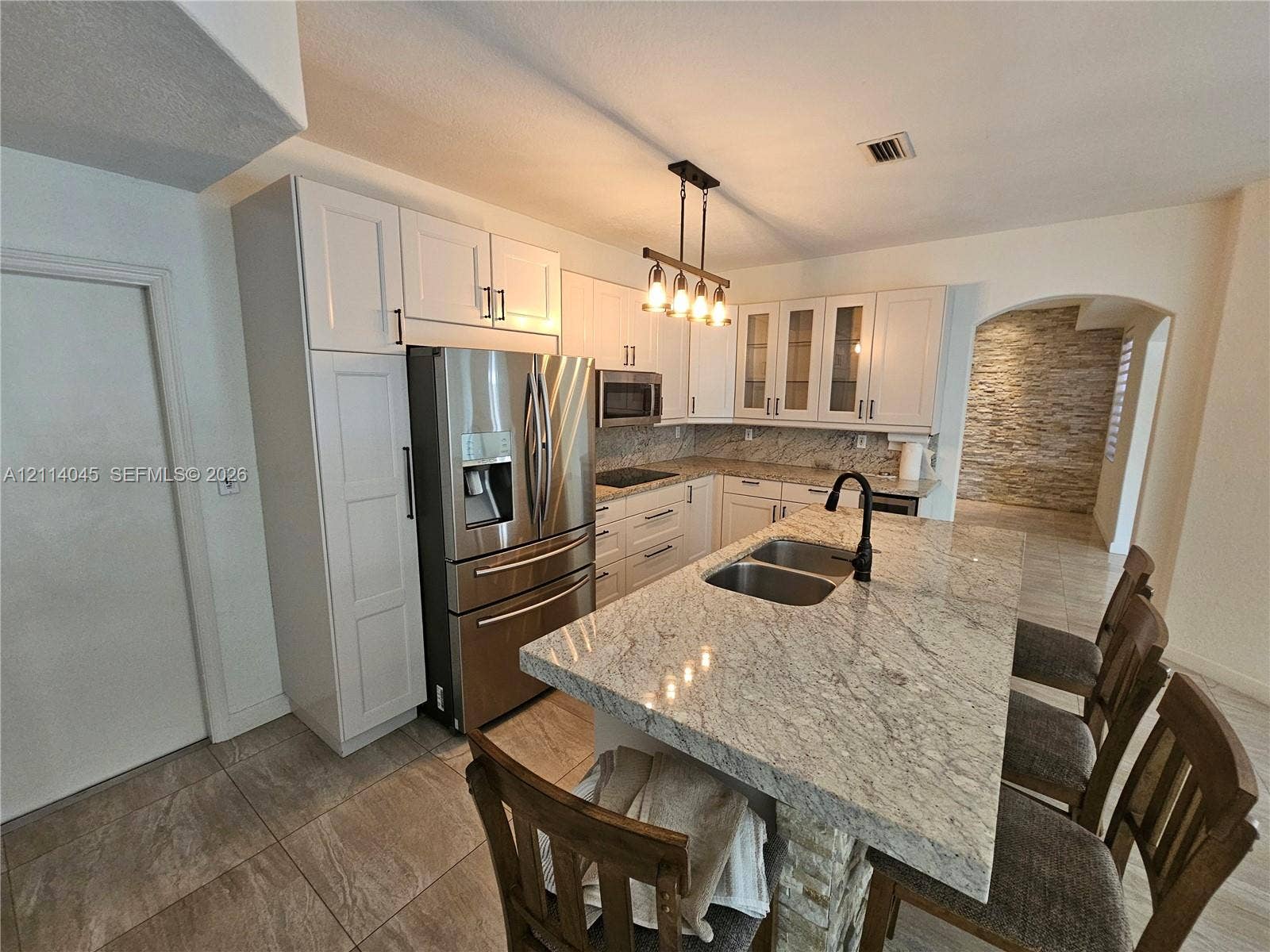 Kitchen featuring white cabinetry, stone-finish countertops, center island with a dual-basin undermount sink, stainless steel appliances, and tile flooring