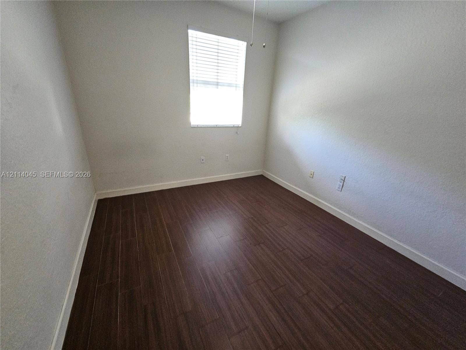 Neutral-toned walls paired with wood-finish flooring and a single-pane window featuring installed blinds