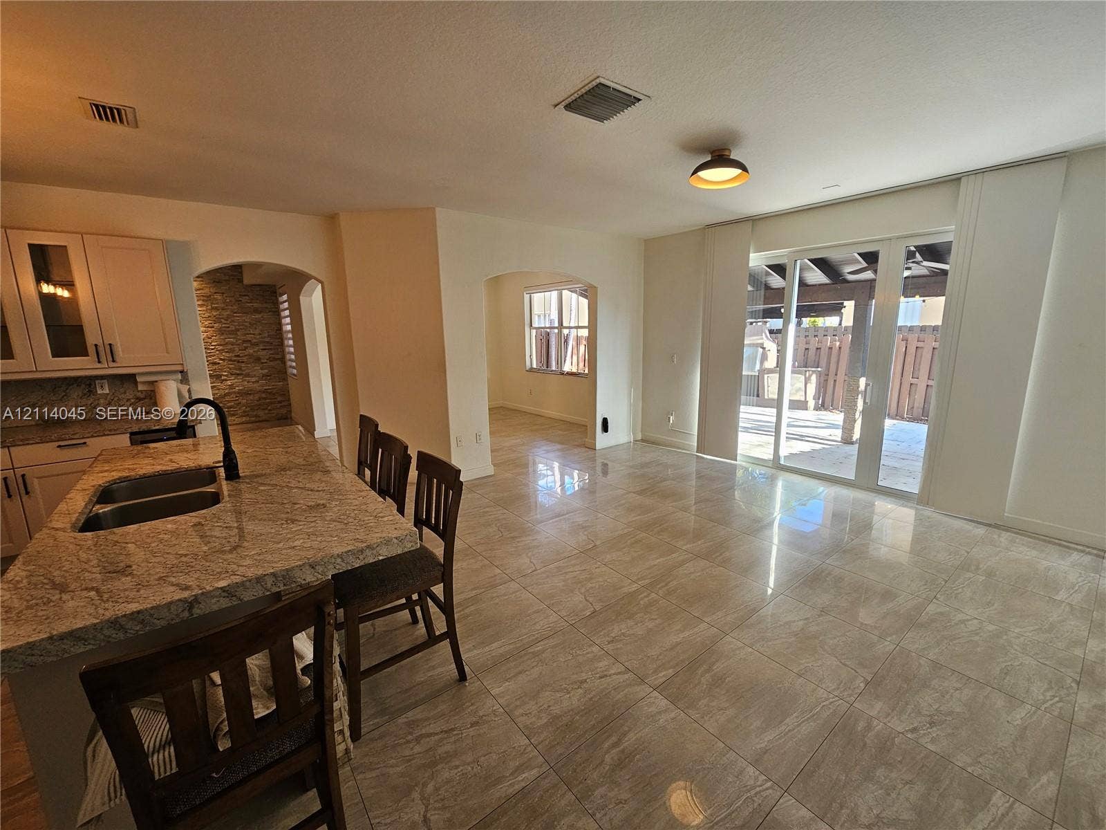 Kitchen featuring a stone-topped island with an integrated double-basin sink and high-arc faucet, neutral tile flooring, arched doorways, and sliding glass doors leading to a covered patio