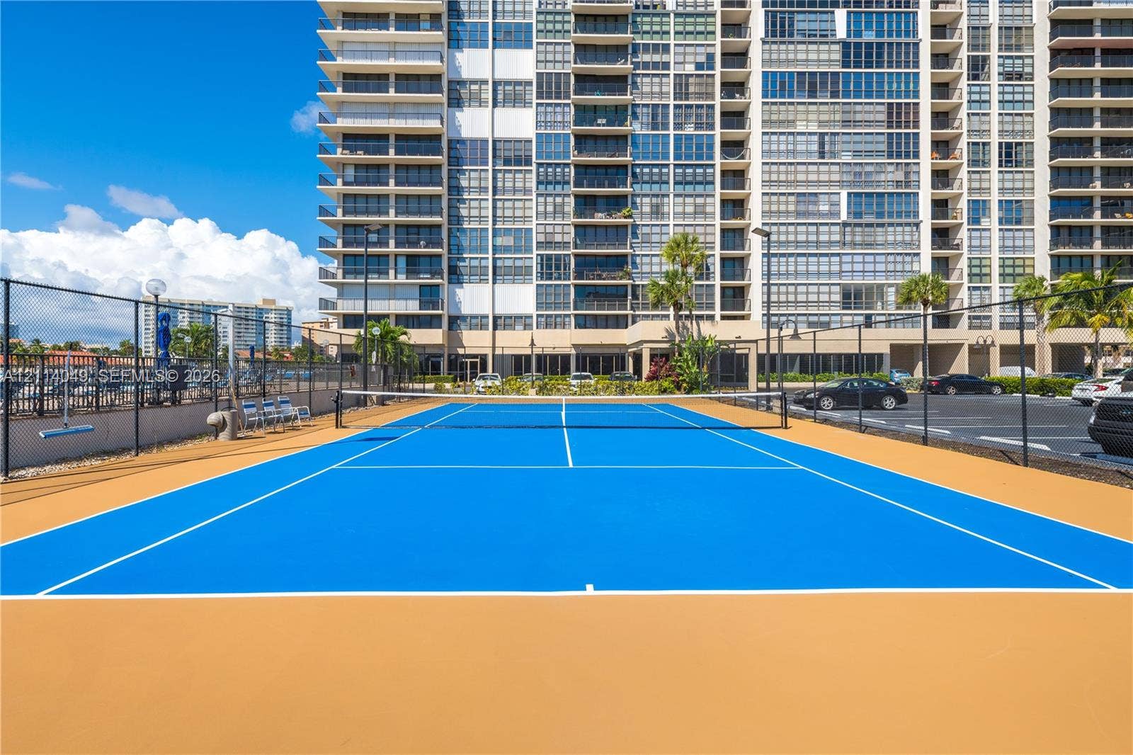 Tennis court featuring a high-contrast blue and tan surface, perimeter chain-link fencing, and exterior light fixtures