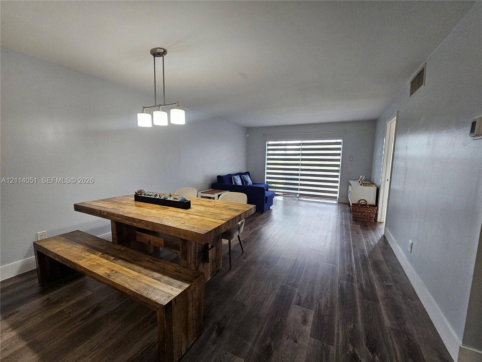 2431 SW 82nd Avenue, #102, Davie, FL 33324 Open-concept interior featuring wood-finish flooring, a three-light pendant fixture, and sliding glass doors with horizontal blinds