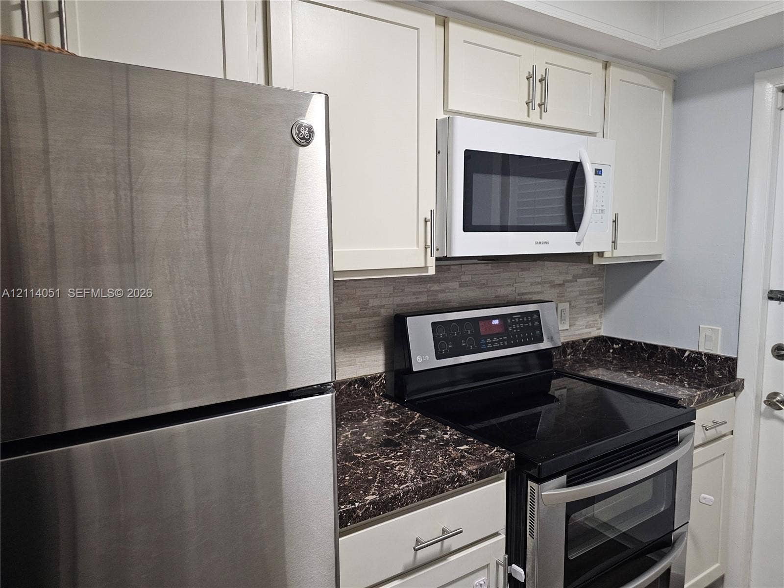 2431 SW 82nd Avenue, #102, Davie, FL 33324 Kitchen featuring white shaker-style cabinetry, stainless steel refrigerator, dark stone-patterned countertops, stacked-tile backsplash, and integrated microwave