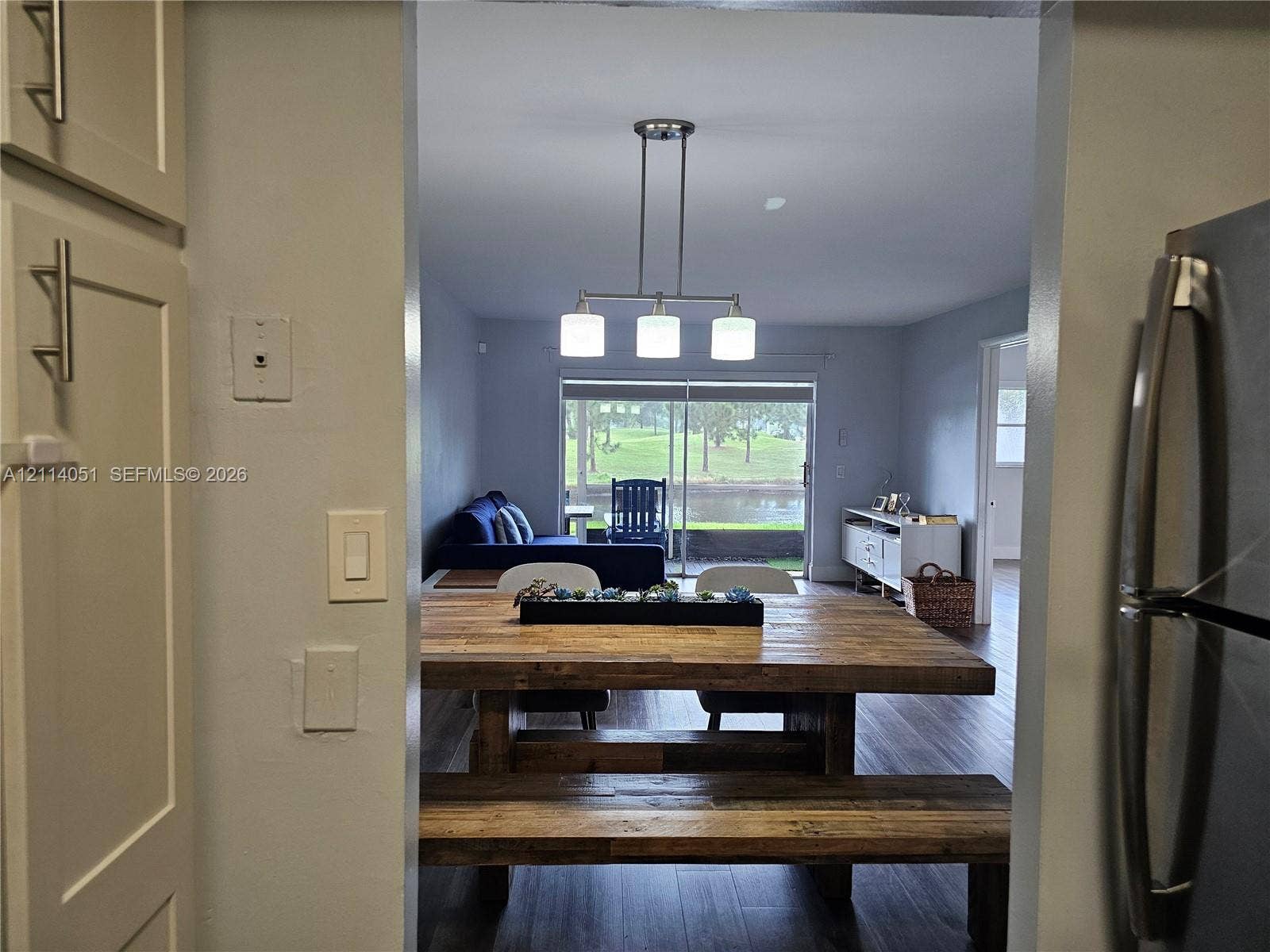 2431 SW 82nd Avenue, #102, Davie, FL 33324 Neutral-toned cabinetry with satin nickel pulls, wood-finish flooring, and a three-light linear pendant fixture, punctuated by sliding glass doors