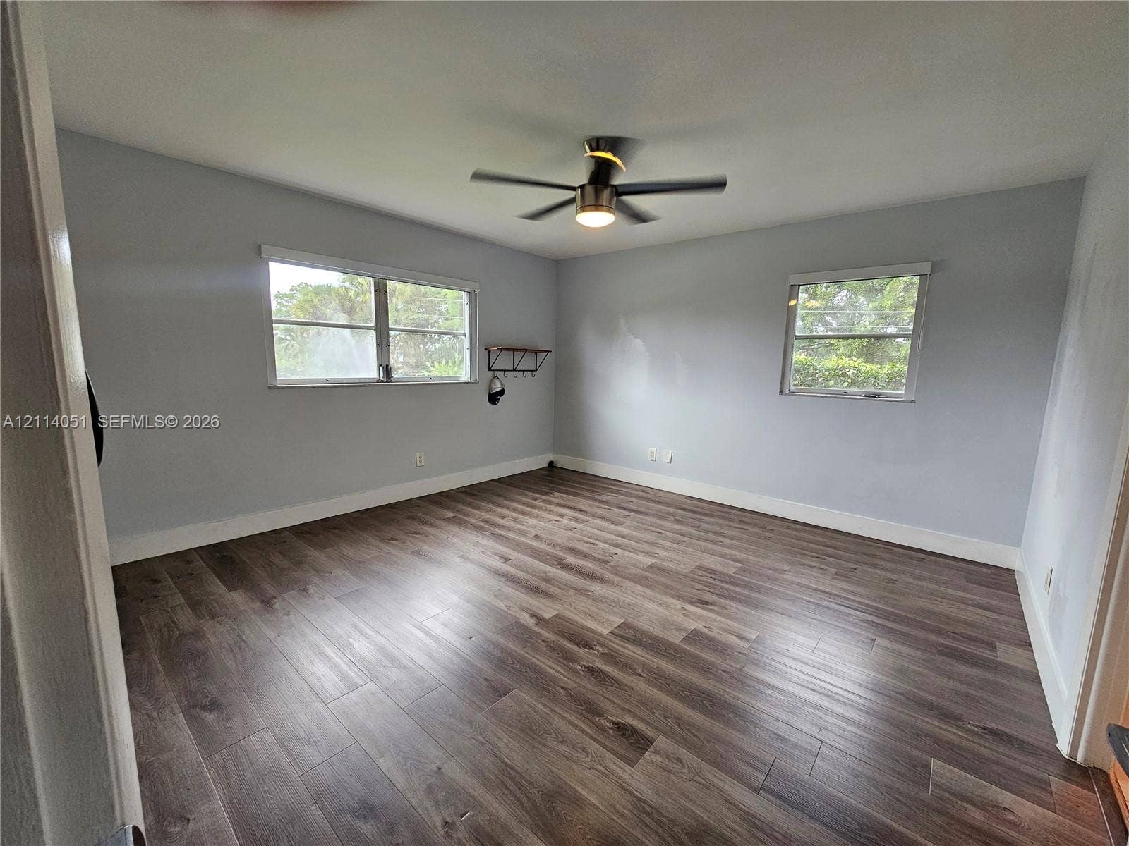 2431 SW 82nd Avenue, #102, Davie, FL 33324 Room featuring wood-finish flooring, two windows with blinds, and a ceiling fan with integrated lighting