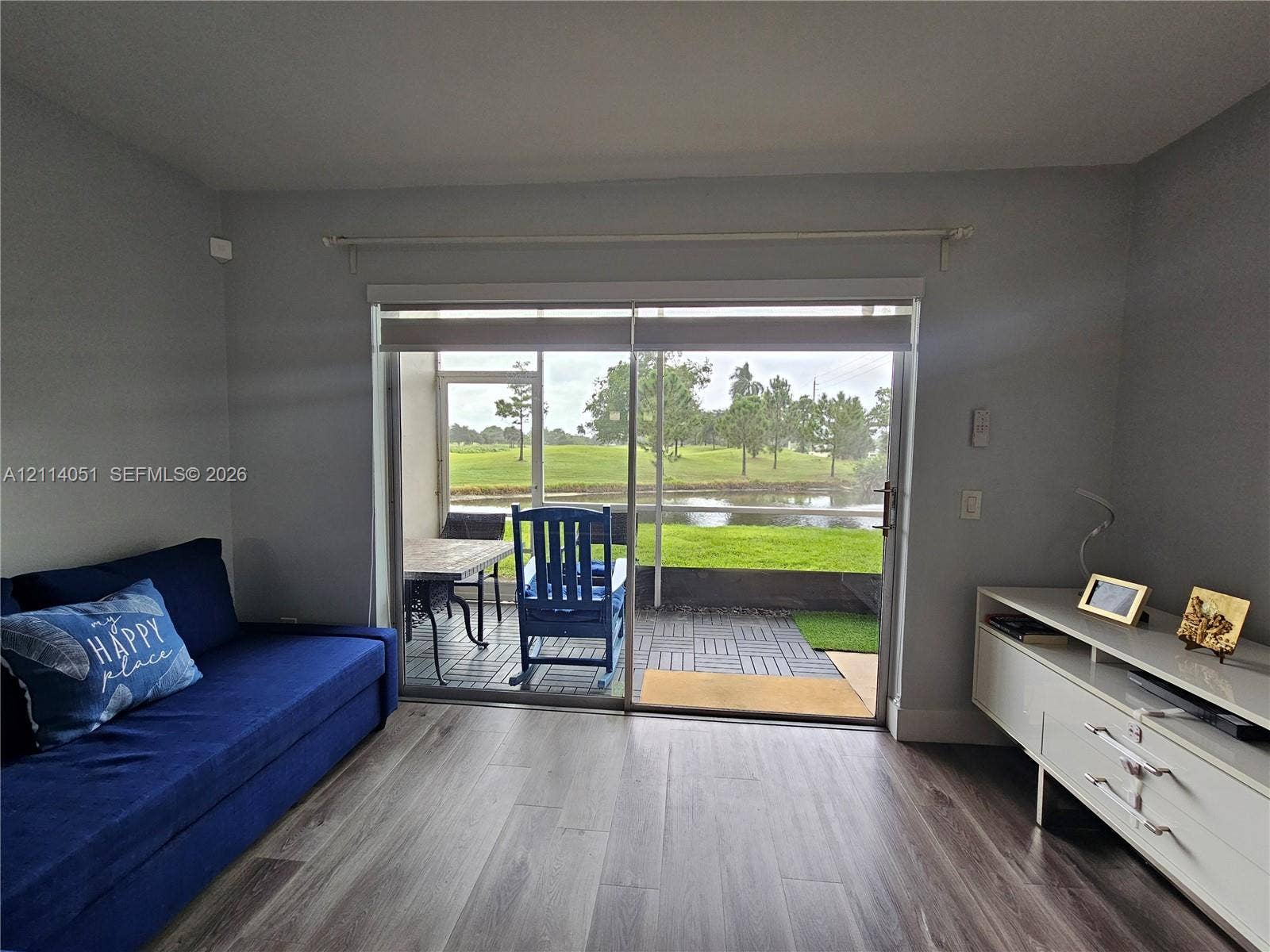 2431 SW 82nd Avenue, #102, Davie, FL 33324 Interior featuring wood-finish flooring, sliding glass doors, and a screen-enclosed patio with interlocking patio tiles overlooking a pond