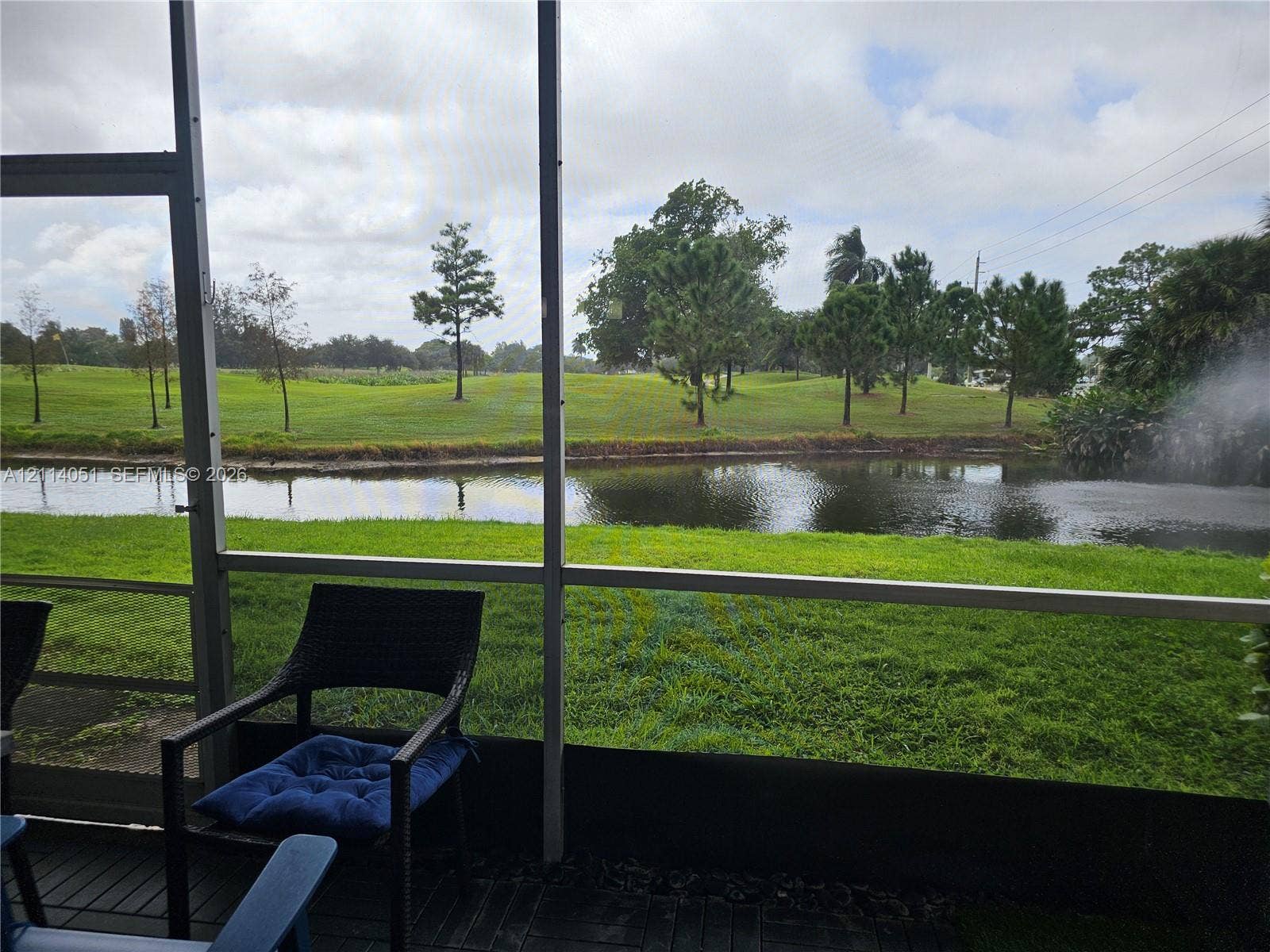 2431 SW 82nd Avenue, #102, Davie, FL 33324 Screened-in patio featuring dark finished decking and a backdrop of a water feature, open green space, and mature trees