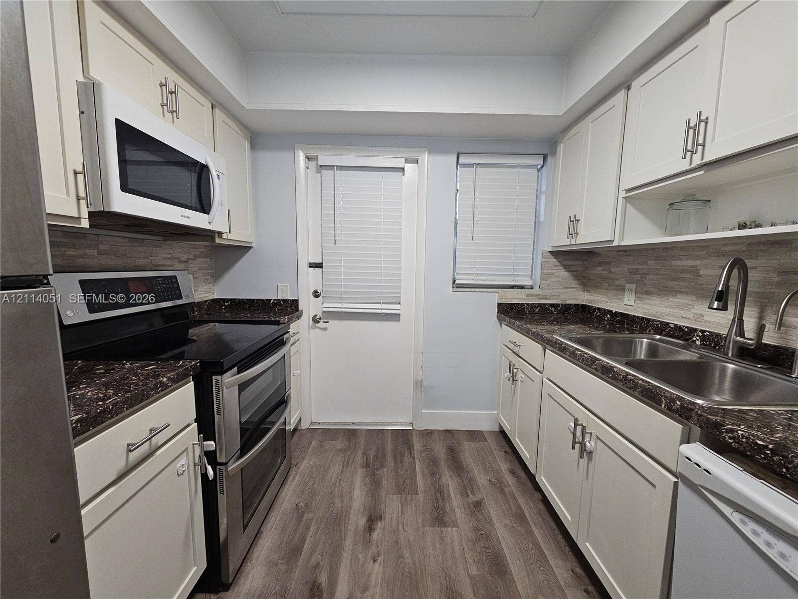 2431 SW 82nd Avenue, #102, Davie, FL 33324 Kitchen featuring shaker-style cabinetry, dark stone-finish countertops, tiled backsplash, stainless steel double-basin sink, and wood-finish flooring
