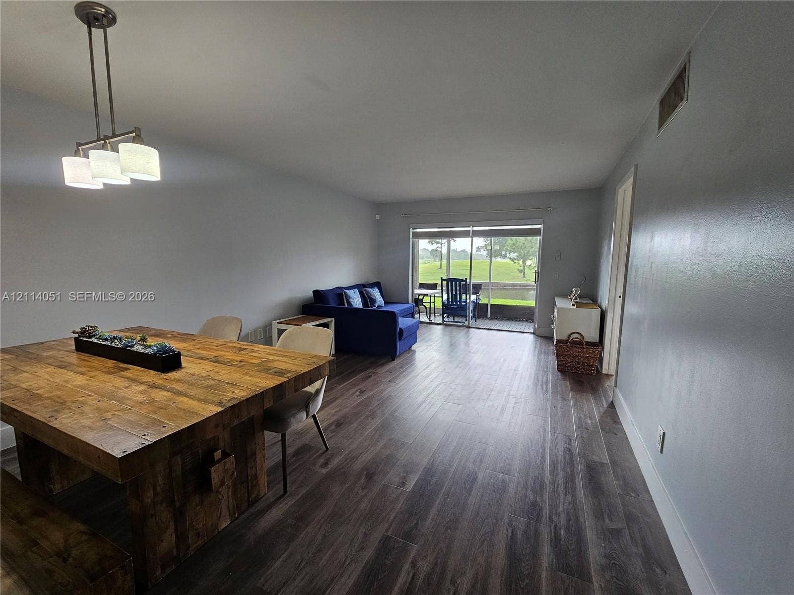 2431 SW 82nd Avenue, #102, Davie, FL 33324 Open-concept space featuring wood-finish flooring, a three-light brushed nickel pendant fixture, and sliding glass doors leading to an exterior screened enclosure