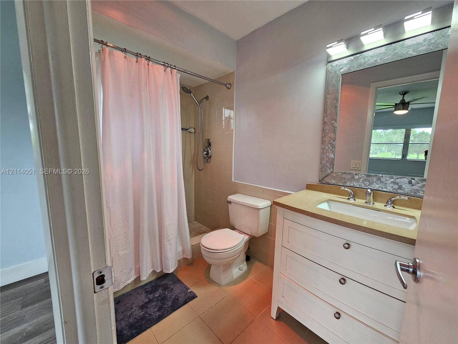 2431 SW 82nd Avenue, #102, Davie, FL 33324 Bathroom featuring a white vanity with three drawers, a neutral-toned countertop with an integrated sink, a framed mirror, a three-bulb light fixture, and a tile-surround shower