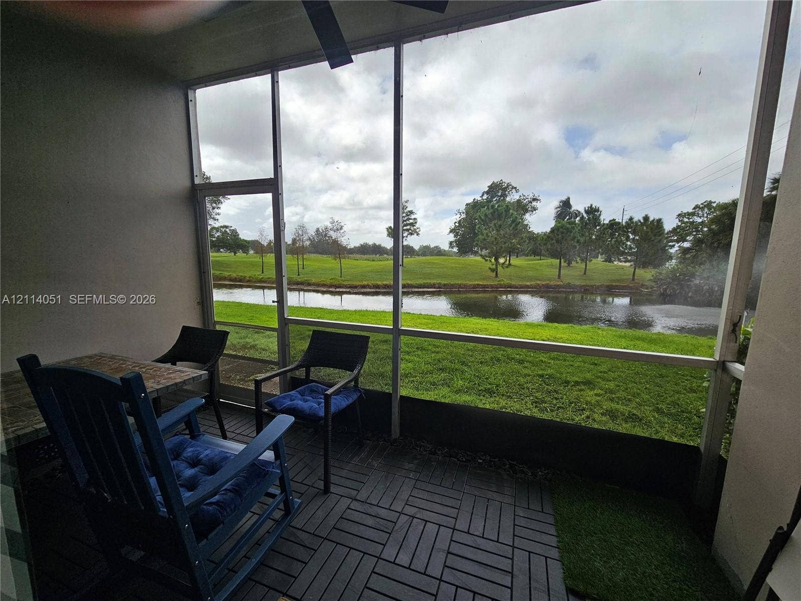 2431 SW 82nd Avenue, #102, Davie, FL 33324 Screen-enclosed porch featuring interlocking deck tiles, ceiling fan, and direct frontage of a pond and green space