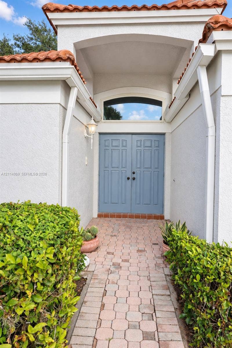 8023 N Tranquility Lake Drive, Delray Beach, FL 33446 Stucco exterior entryway featuring a terracotta tile roof, arched transom window, dual panel doors, and a decorative wall-mounted lantern