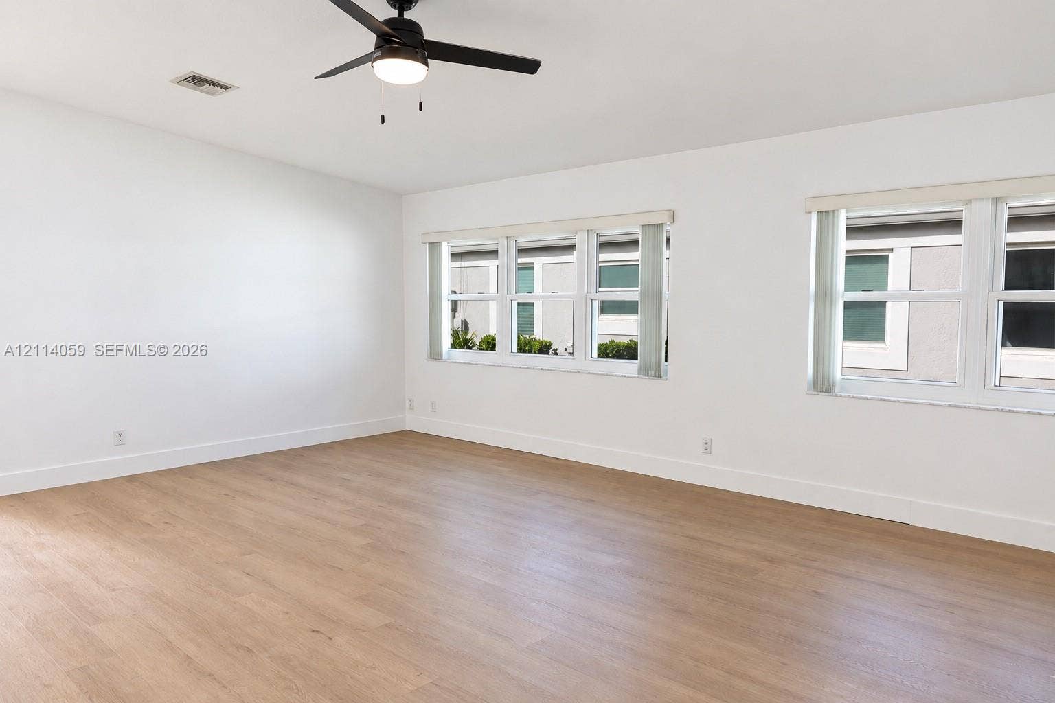 8023 N Tranquility Lake Drive, Delray Beach, FL 33446 Neutral-toned interior space featuring wood-finish flooring, dual windows, and a matte black ceiling fan with integrated lighting