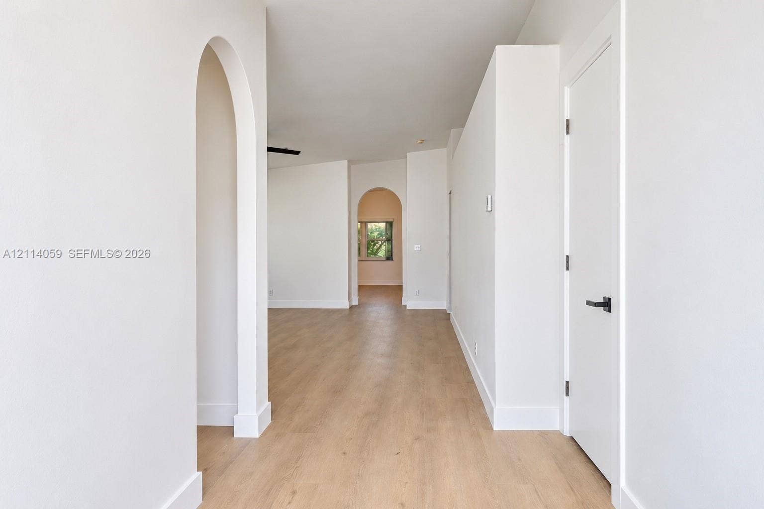 8023 N Tranquility Lake Drive, Delray Beach, FL 33446 Interior space featuring arched doorways, wood-finish flooring, and minimalist white walls with matte black hardware