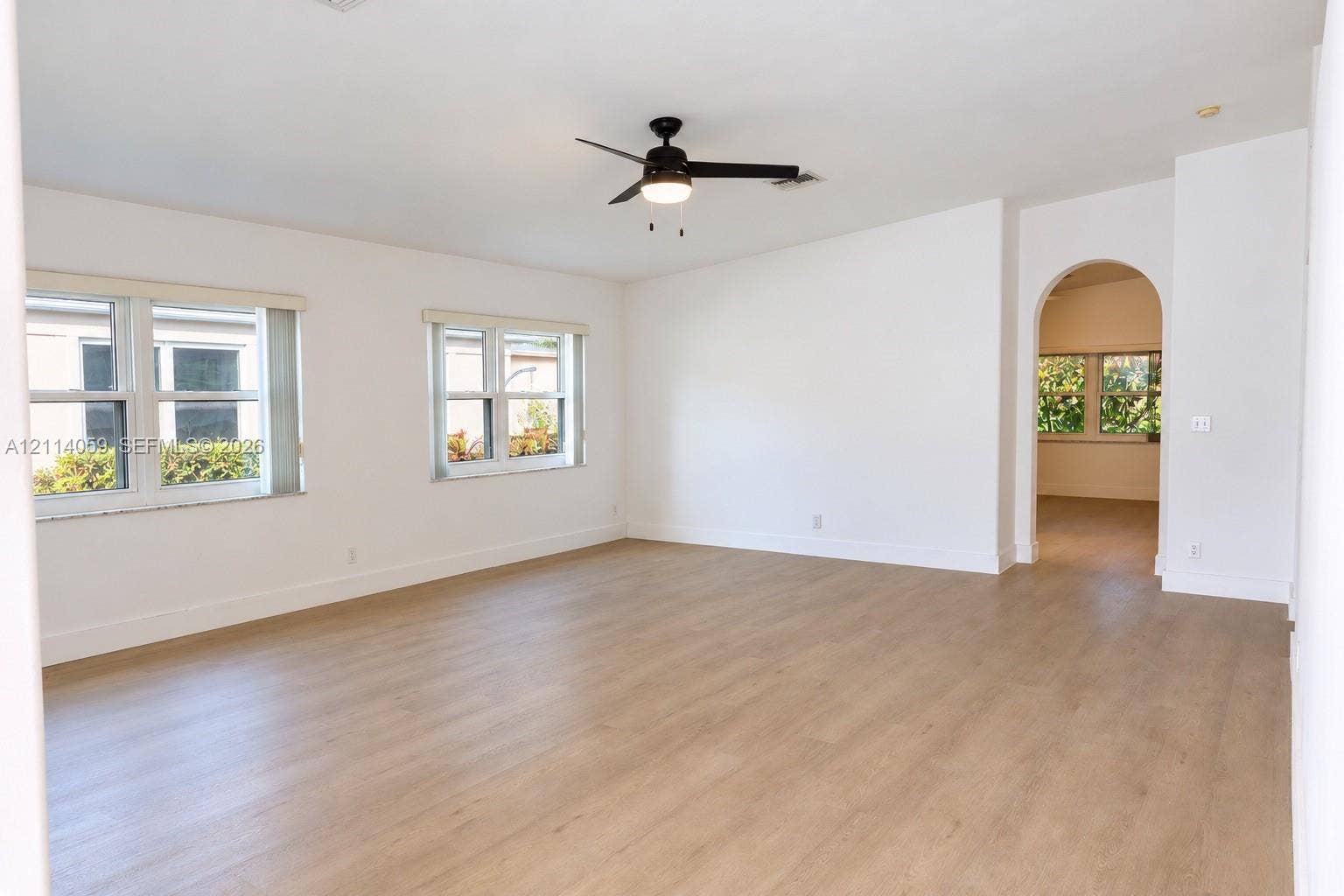 8023 N Tranquility Lake Drive, Delray Beach, FL 33446 Open interior space featuring wood-finish flooring, an arched entryway, dual windows, and a ceiling fan with integrated lighting